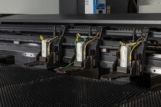 Close-up of the three programmable work clamps on their rail at the edge of the brush table